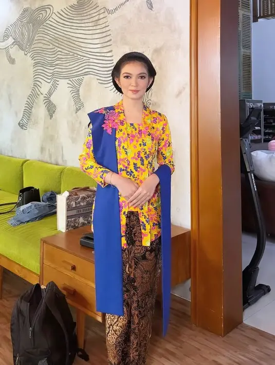 Selvi Ananda tampil elegan dengan kebaya kuning kutu baru motif bunga colorful. Dipadukan selendang biru dan kain batik lilit coklat sebagai bawahan. [@selvie_ananda_]