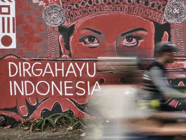 Pengendara motor melintasi mural bertema HUT ke-75 RI di Jalan Abdullah Syafei, Jakarta, Minggu (16/8/2020). Jelang HUT ke-75 RI, mural bernuansa Merah Putih banyak menghiasi jalanan Ibu Kota guna memberi semangat nasionalisme kepada warga di tengah pandemi COVID-19. (merdeka.com/Iqbal S.Nugroho)