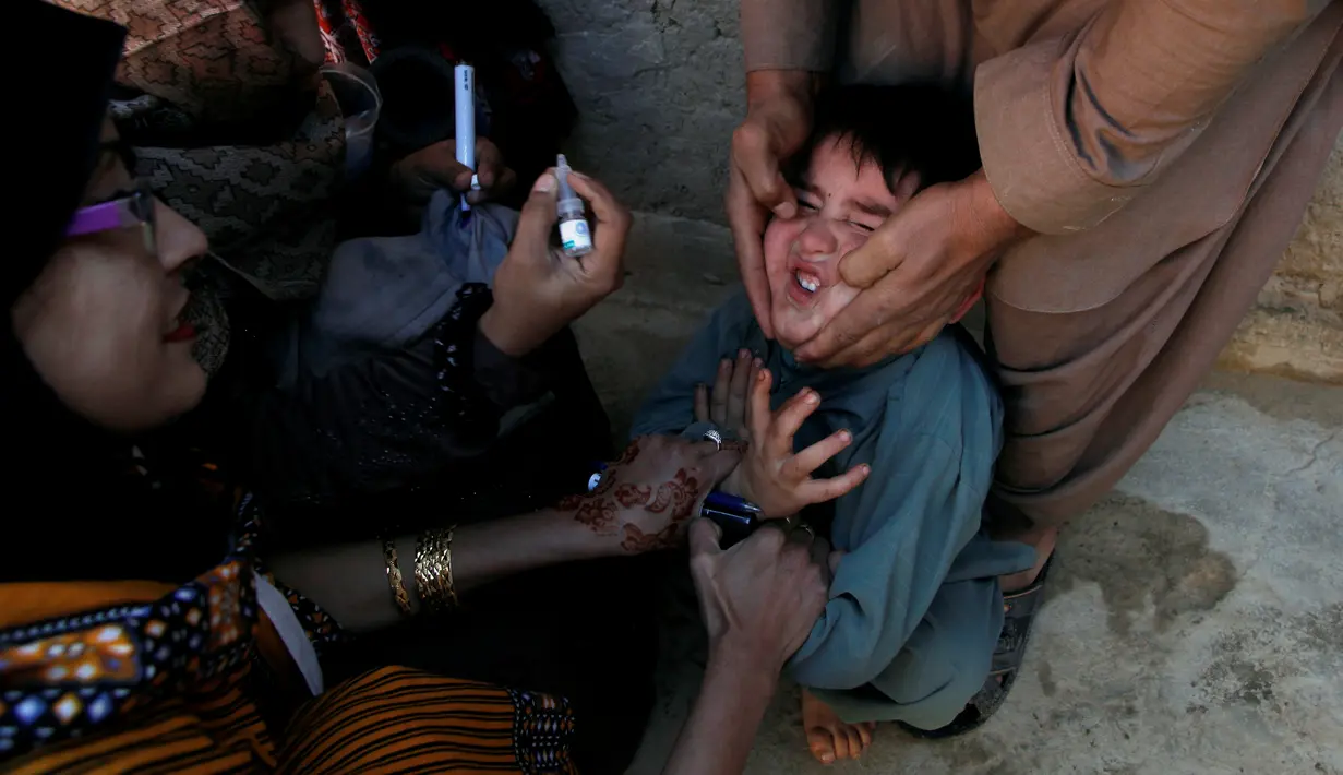 Seorang anak dipegangi orang tuanya saat petugas memberikan imunisasi polio di sepanjang jalan di Quetta, Pakistan, Senin (2/1). (REUTERS/Naseer Ahmed)