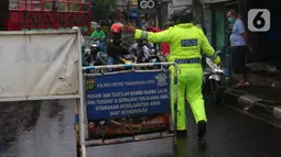 Petugas kepolisian mengatur lalu lintas saat melakukan penutupan jalan KH Hasyim Ashari, Kota Tangerang, Banten, Sabtu (16/7/2022). Akibat banjir yang merendam kawasan tersebut membuat petugas harus menutup jalur dan memutarbalikan para pengendara yang melintas. (Liputan6.com/Angga Yuniar)