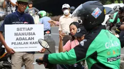 Aktivis Koalisi Pejalan Kaki (KPK) membawa poster himbauan saat menghadang pengendara sepeda motor yang menerobos trotoar di depan Tempat Pemakaman Umum (TPU) Menteng Pulo, Jalan Casablanca, Jakarta Selatan, Jumat (21/7). (Liputan6.com/ Immanuel Antonius)