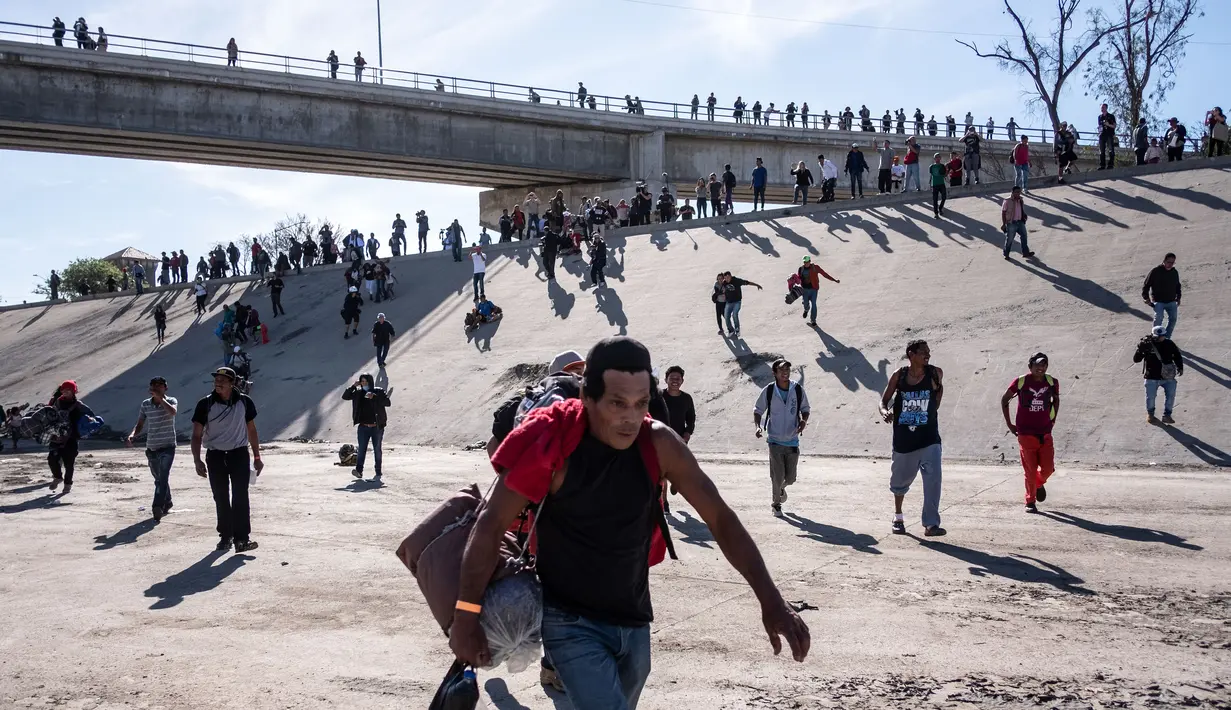 Sekelompok migran berlari di sepanjang sungai kering Sungai Tijuana dalam upaya untuk sampai ke pelabuhan masuk El Chaparral, di Tijuana, Baja California State, Meksiko, dekat perbatasan AS-Meksiko (25/11). AFP Photo/Guillermo Arias)