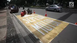 Pekerja menyelesaikan pengecatan rambu jalur kuning khusus sepeda motor di Jalan Medan Merdeka, Jakarta, Selasa (16/1).  Nantinya, pemotor hanya boleh melintas kawasan ini melalui jalur mengikuti jalan bercat kuning tersebut. (Liputan6.com/Arya Manggala)
