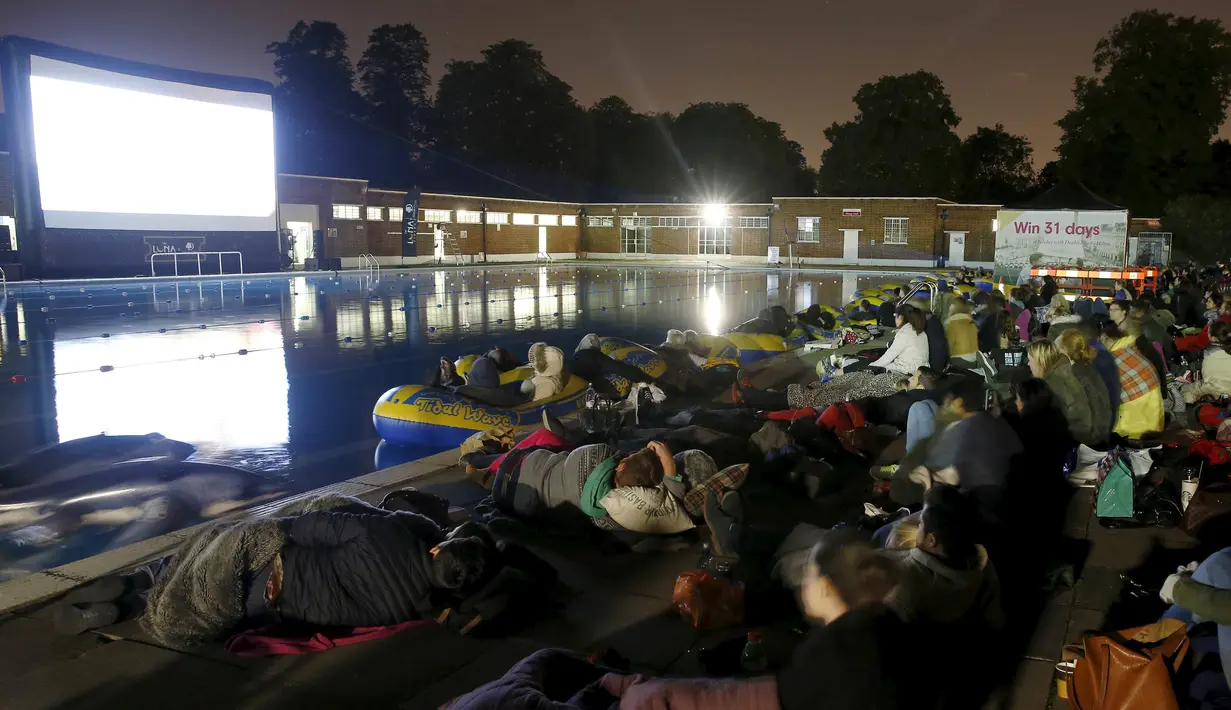Sejumlah Penonton serius menyaksikan pemutaran film "Jaws" di pinggir kolam renang dan ada juga yang mengunakan ban karet di Brockwell Lido, London, Inggris, Kamis (17 /9/2015). (REUTERS/Luke MacGregor)