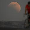 Gerhana bulan terlihat di belakang pengendara sepeda saat blood moon pertama tahun ini di Irwindale, California, Amerika Serikat, Minggu (15/5/2022). (AP Photo/Ringo H.W. Chiu)