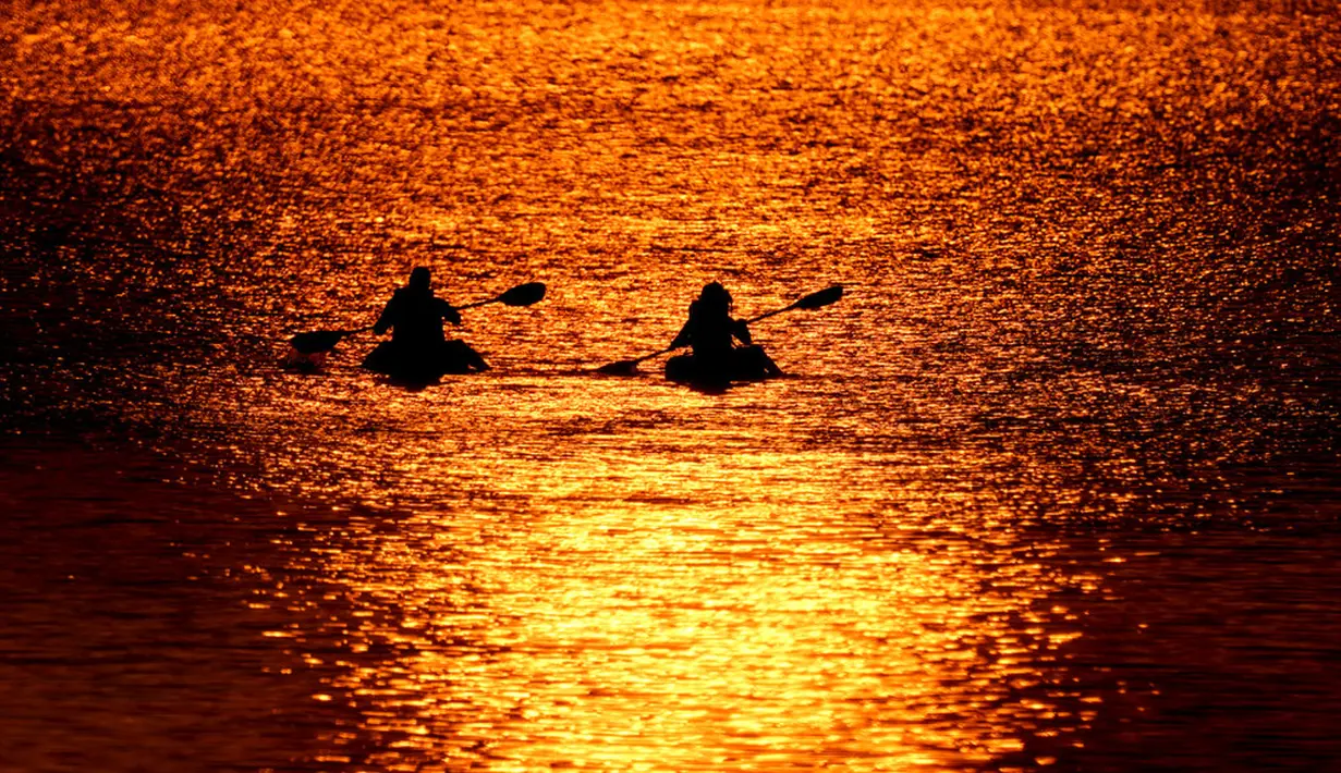 Orang-orang menyaksikan matahari terbenam sambil berperahu di Shawnee Mission Lake, Shawnee, Kansas, Amerika Serikat, Jumat (9/10/2020). Matahari terbenam terus lebih cerah dari biasanya karena asap dari kebakaran hutan barat terus melayang di seluruh negeri. (AP Photo/Charlie Riedel)
