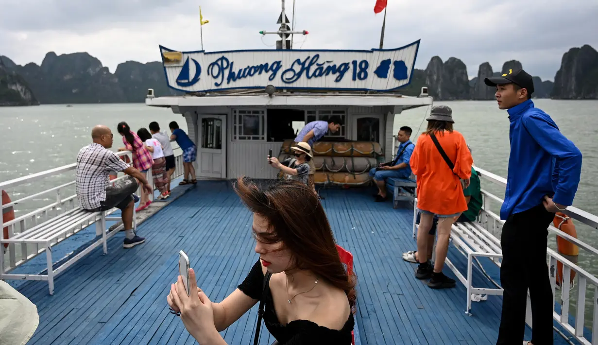<p>Wisatawan domestik berpose untuk foto di atas kapal di tengah Ha Long Bay, Quang Ninh, Vietnam, (16/5/2020). Sempat terpukul akibat pandemi virus corona Covid-19, pariwisata Vietnam kembali menggeliat setelah otoritas setempat melonggarkan pembatasan perjalanan. (AFP/Manan Vatsyayana)</p>
