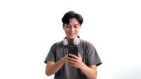 Seorang pria memakai headphone sedang mendengarkan musik melalui aplikasi di ponsel. (Depositphoto/wichayada69@gmail.com)