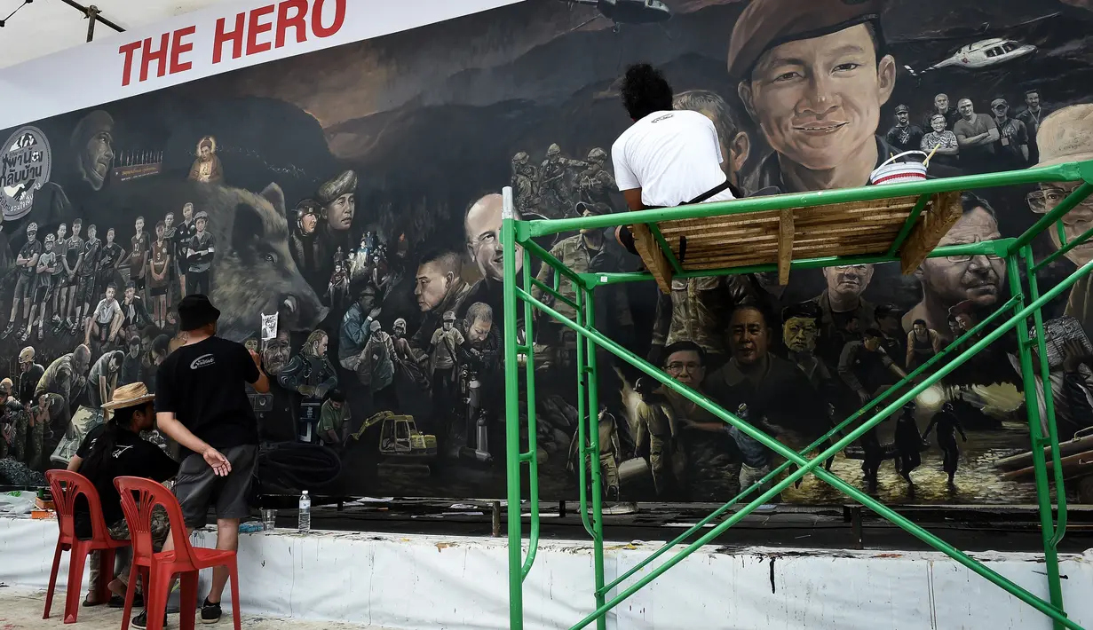 Seniman lokal menyelesaikan mural berjudul 'The Heroes' di Chiang Rai, 18 Juli 2018. Tampak lukisan wajah Saman Gunan, mantan penyelam AL Thailand yang meninggal dunia saat membantu operasi penyelamatan tim sepak bola Wild Boars. (AFP/Lillian SUWANRUMPHA)