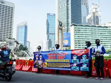 Petugas kepolisian membentangkan spanduk saat sosialisasi pelaksanaan ganjil genap di Kawasan Bundaran HI, Jakarta, Minggu (2/8/2020). Ditlantas Polda Metro Jaya kembali memberlakukan sistem ganjil genap di 25 ruas jalan protokol  DKI Jakarta mulai Senin, 3 Agustus 2020. (Liputan6.com/Faizal Fanani)