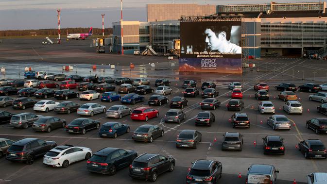 Orang-orang duduk di mobil mereka saat menonton film di bioskop drive-in di area apron bandara kota Vilnius, Lithuania pada 29 April 2020. Bandara tersebut kini sepi penumpang, akibat pembatasan perjalanan internasional untuk mengatasi penyebaran virus corona covid-19. (AP/Mindaugas Kulbis)