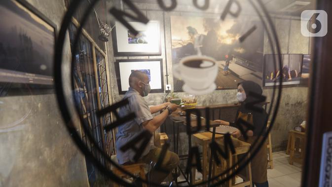 Pengunjung menikmati kopi di kedai Ngopi di Halaman Jalan Pulo Kamboja, Kebayoran Lama, Jakarta, Selasa (12/01/2021). Kedai yang buka pada hari Selasa - Minggu dari pukul 10.00 - 22.00 WIB juga menawarkan koleksi buku fotografi yang dibaca di tempat. (Liputan6.com/Fery Pradolo)