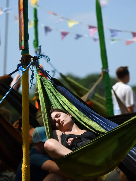Seorang wanita beristirahat di tempat tidur gantung saat mereka menghadiri festival Glastonbury di desa Pilton, di Somerset, Inggris Barat Daya (22/6/2022). Pandemi virus corona memaksa penyelenggara untuk membatalkan acara dua tahun terakhir, dan mereka yang pergi tahun ini menghadapi perjalanan yang sulit melawan tiga hari pemogokan kereta api besar di seluruh negeri. (AFP/Andy Buchanan)