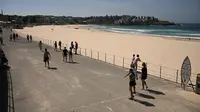 Orang-orang berjalan melewati Pantai Bondi yang kosong setelah ditutup oleh pihak berwenang di Sydney, Minggu (22/3/2020). Otoritas Australia menutup Bondi Beach  lantaran orang-orang mengabaikan larangan tidak berkumpul dalam jumlah besar untuk menekan penyebaran virus corona. (PETER PARKS/AFP)