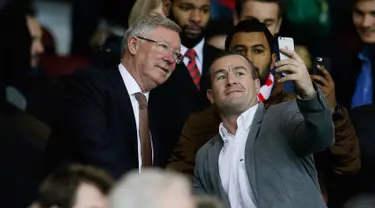Mantan manajer Manchester United Sir Alex Ferguson berselfie dengan fans saat menyaksikan pertandingan antara Manchester United dengan Chelsea di Stadion Old Trafford, Inggris (28/12). MU bermain imbang dengan Chelsea dengan skor 0-0. (Reuters/Phil Noble)