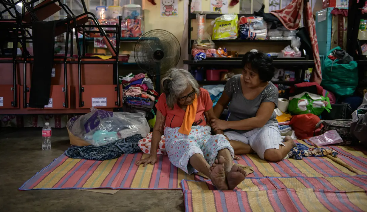 Wanita lanjut usia dibantu kerabatnya saat berada di pusat evakuasi korban letusan Gunung Taal di Sekolah Dasar Dona Tiburcia Carpio Malvar, Tanauan, Filipina, Rabu (16/1/2020). Pihak berwenang Filipina memperingatkan bahwa potensi Gunung Taal untuk kembali meletus masih tinggi. (Ed JONES/AFP)