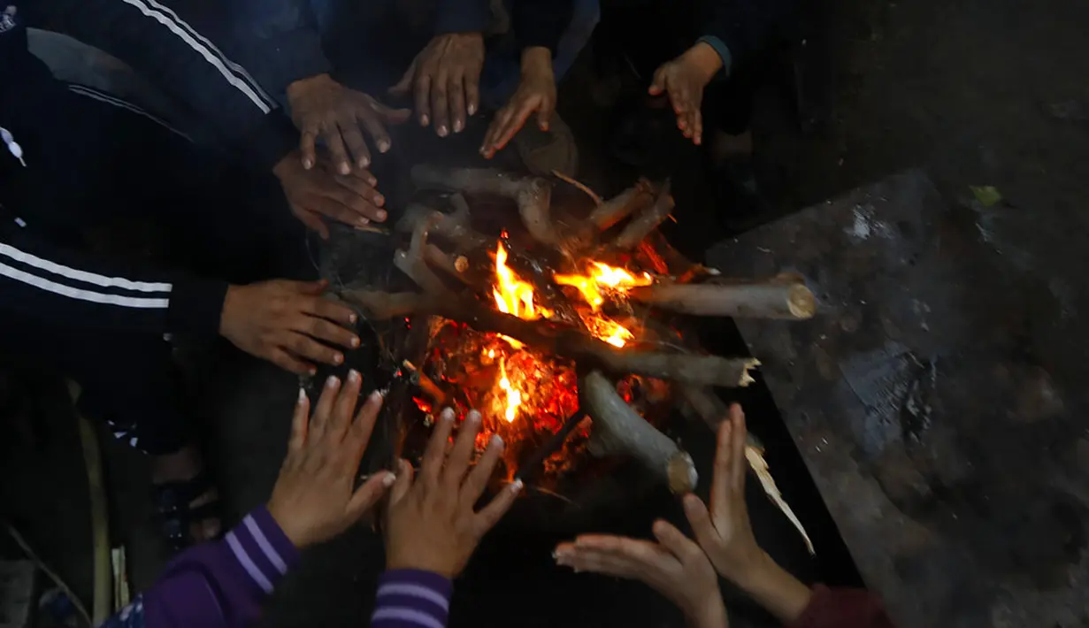 Sebuah keluarga duduk sekitar kayu bakar perapian rumah mereka saat cuaca dingin di daerah kumuh Kota Gaza, Palestina, 27 Januari 2022. (AP Photo/Hatem Moussa)