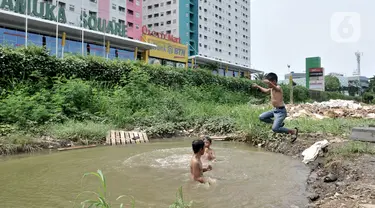 Anak-anak berenang di kubangan air di depan Apartemen Green Pramuka, Jakarta, Rabu (5/2/2020). Keterbatasan ekonomi dan minimnya lahan bermain membuat sekelompok anak sekolah dasar ini memilih berenang di kubangan meskipun mereka tahu air kotor dapat menimbulkan penyakit. (merdeka.com/Iqbal Nugroho)