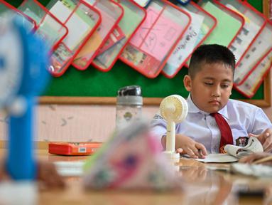 Seorang siswa sekolah dasar menggunakan kipas angin portabel untuk menyejukkan ruangan kelas saat cuaca panas di Banda Aceh pada 15 Mei 2023. (AFP/CHAIDEER MAHYUDDIN)