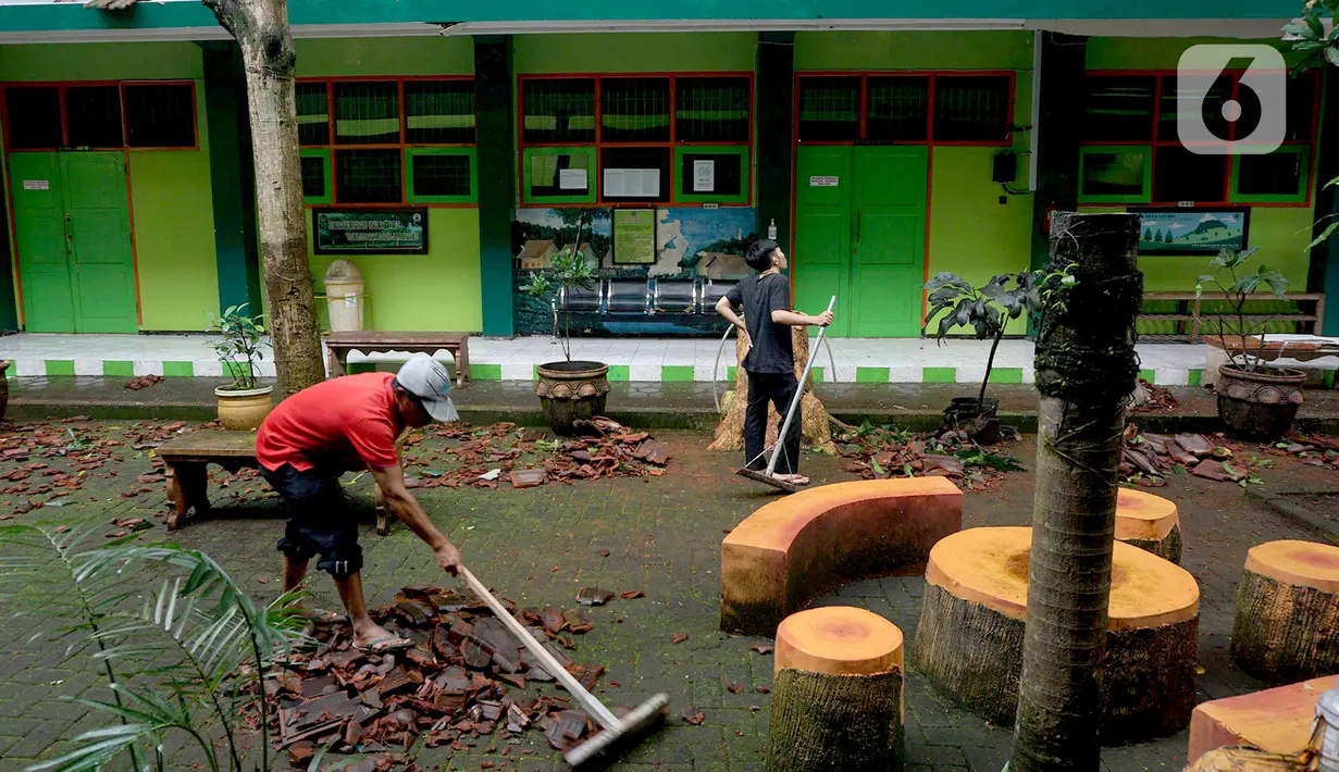 Pekerja membersihkan reruntuhan genting yang memenuhi halaman sekolah akibat gempa di SMK Negeri 1 Turen, Malang, Jawa Timur, Minggu (11/4/2021). Gempa yang mengguncang kawasan Malang dan sekitarnya membuat sejumlah bangunan rusak. (merdeka.com/Nanda F. Ibrahim)