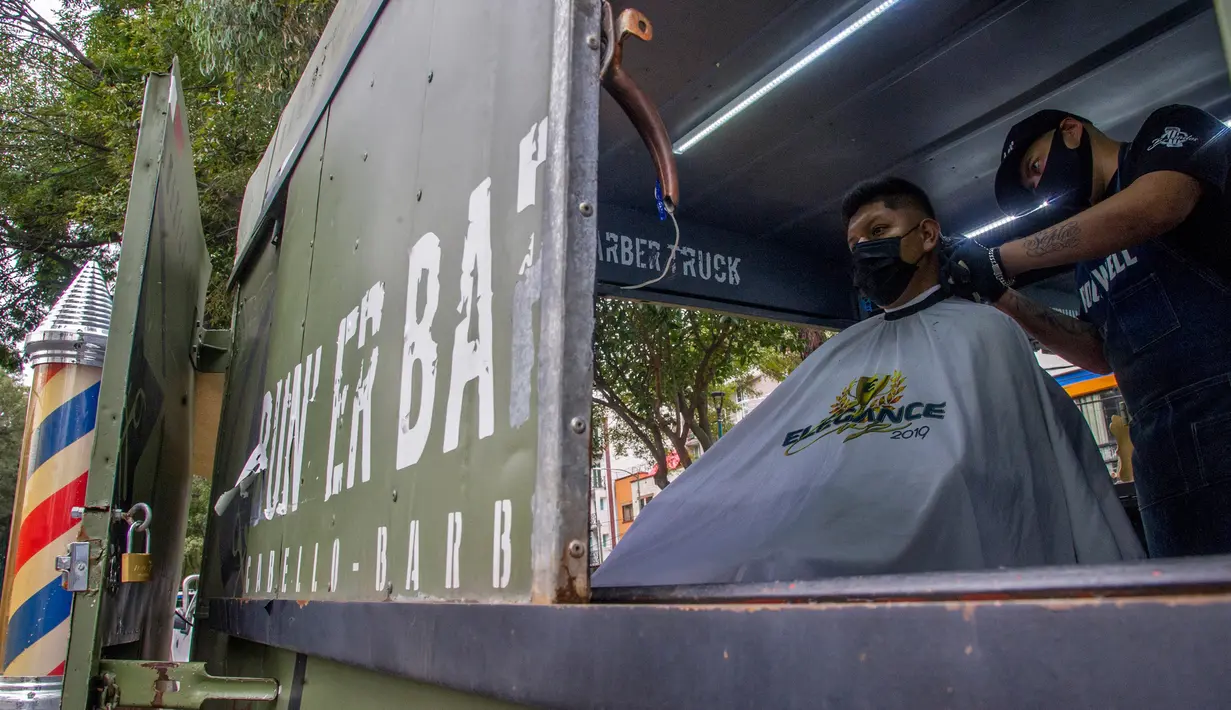 Seorang tukang cukur memotong rambut pelanggan di mobil van atau truck yang diubah menjadi barbershop di sebuah jalan di tengah pandemi virus corona COVID-19, di Mexico City, pada Minggu (6/9/2020). (Photo by CLAUDIO CRUZ / AFP)