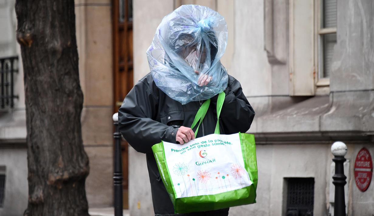 Seorang pria melindungi wajahnya dengan kantong plastik saat diberlakukannya lockdown untuk menghentikan penyebaran COVID-19 di jalanan Paris pada 21 Maret 2020. Masker dijadikan masyarakat pilihan untuk mencegah penyebaran virus corona yang terus meningkat di seluruh dunia. (FRANCK FIFE/AFP)