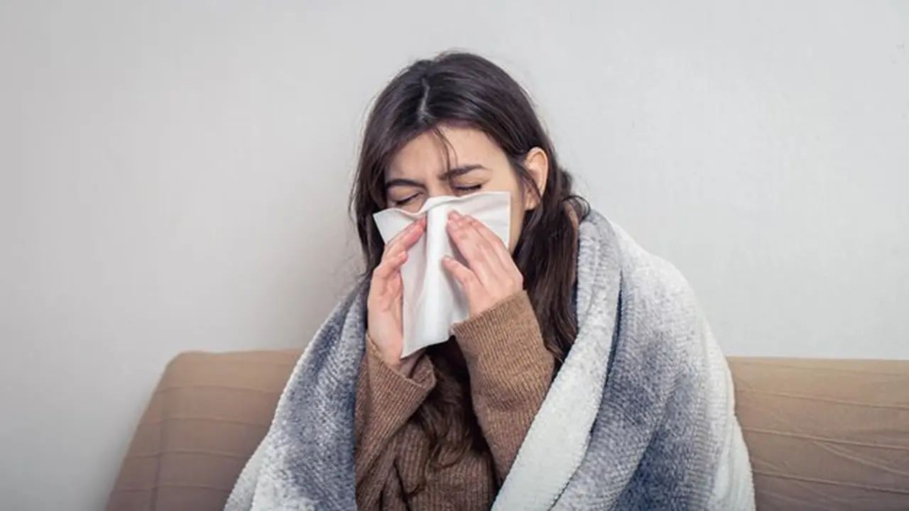 Seorang perempuan yang sedang terserang flu menyelimuti tubuhnya di atas sofa dan menutup hidungnya menggunakan tisu (Foto Dok: Freepik/pvproductions)