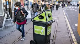 Pejalan kaki berjalan melewati tempat sampah untuk masker sekali pakai, di Aarhus Center, Denmark, Senin (23/11/2020). Kota Aarhus menempatkan seratus tempat sampah khusu berukuran 240 liter yang dapat menampung sekitar 3000 masker bekas. (Henning Bagger/Ritzau Scanpix/AFP)