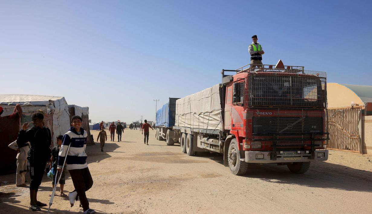 Sebelum Israel melancarkan perang di Gaza, Rafah merupakan jalur penyeberangan utama orang-orang yang keluar masuk wilayah Palestina. Tampak dalam foto, warga Palestina menyaksikan truk-truk yang membawa bantuan kemanusiaan tiba di Khan Yunis di Jalur Gaza selatan, setelah melewati penyeberangan perbatasan Rafah dari Mesir, pada 1 Februari 2026. (Bashar Taleb/AFP)