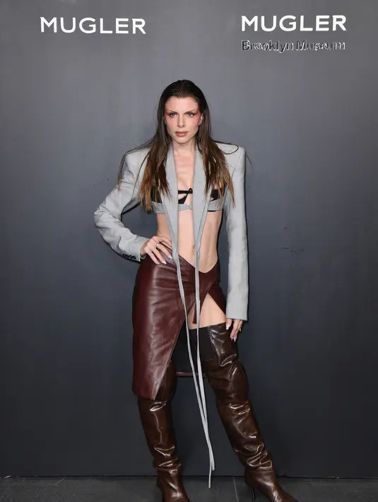 Julia Fox berpose saat menghadiri Pembukaan Pameran Mugler Couturissime di Museum Brooklyn  di New York City pada 15 November 2022. Julia menambahkan bralette hitam di bawah jaket Mugler lengan panjang, dan memadukan atasannya dengan rok cokelat berpinggang rendah dengan belahan yang sangat tinggi di sisi kiri. Potongan kain yang panjang dan tipis jatuh dari kerah blazer ke bawah menuju sepatu bot bertumit di atas lututnya yang berwarna cokelat. (AFP/ANGELA WEISS)