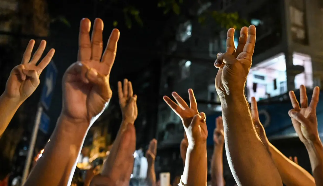 Orang-orang memberi hormat tiga jari setelah seruan untuk protes keluar di media sosial di Yangon, Myanmar, 3 Februari 2021. Kudeta militer Myanmar terus memicu protes warga dengan membunyikan klakson mobil, menyalakan lampu ponsel, dan memukul-mukul panci. (STR/AFP)