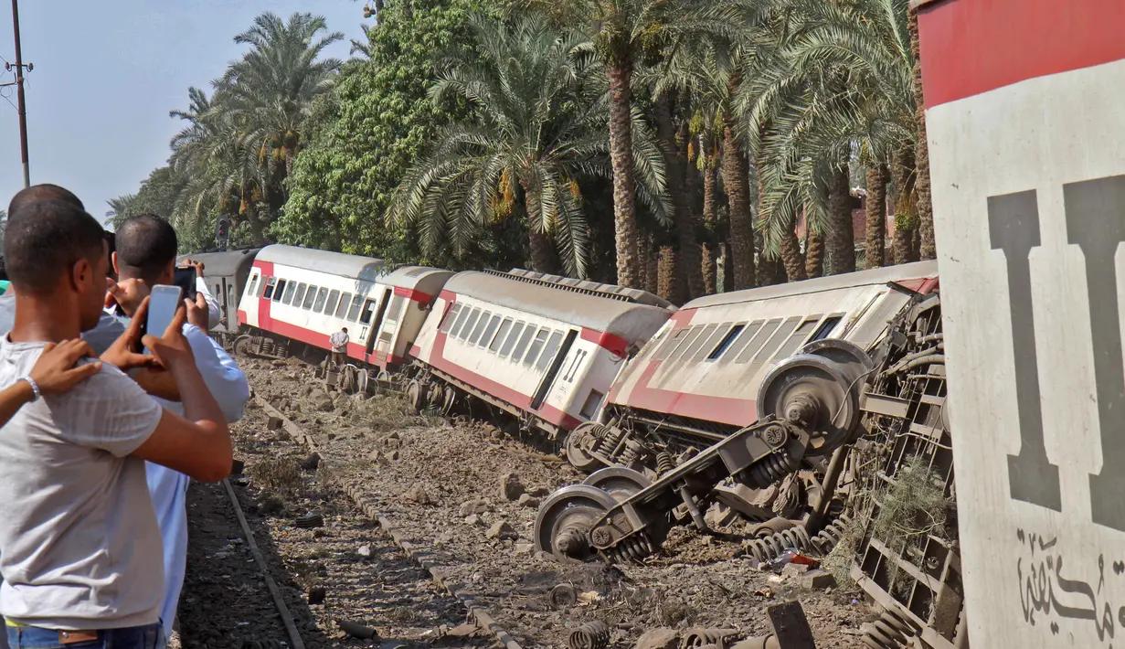 Sejumlah warga mengabadikan gerbong kereta usai tergelincir saat melintasi jalur di daerah al-Badrasheen, Giza, Mesir, (13/7). Dalam kejadian tersebut, tidak ada korban jiwa dan sekitar 55 penumpang terluka. (AFP Photo/Stringer)