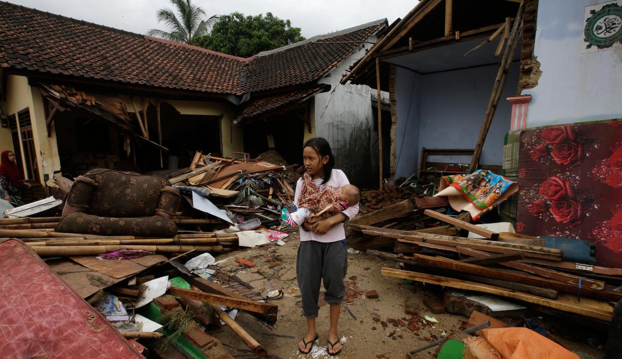 Seorang gadis menggendong bayi berjalan di dekat puing-puing di daerah yang dilanda tsunami di Carita, Banten, Kamis, (27/12). (AP Photo/Achmad Ibrahim)