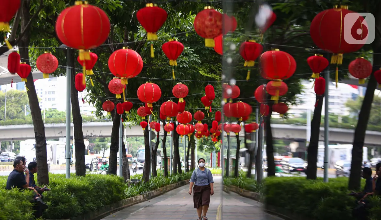 Warga melintas di bawah lampu lampion merah yang terpasang di trotoar kawasan jalan Jenderal Sudirman, Jakarta, Kamis (15/1/2025). (Liputan6.com/Angga Yuniar)