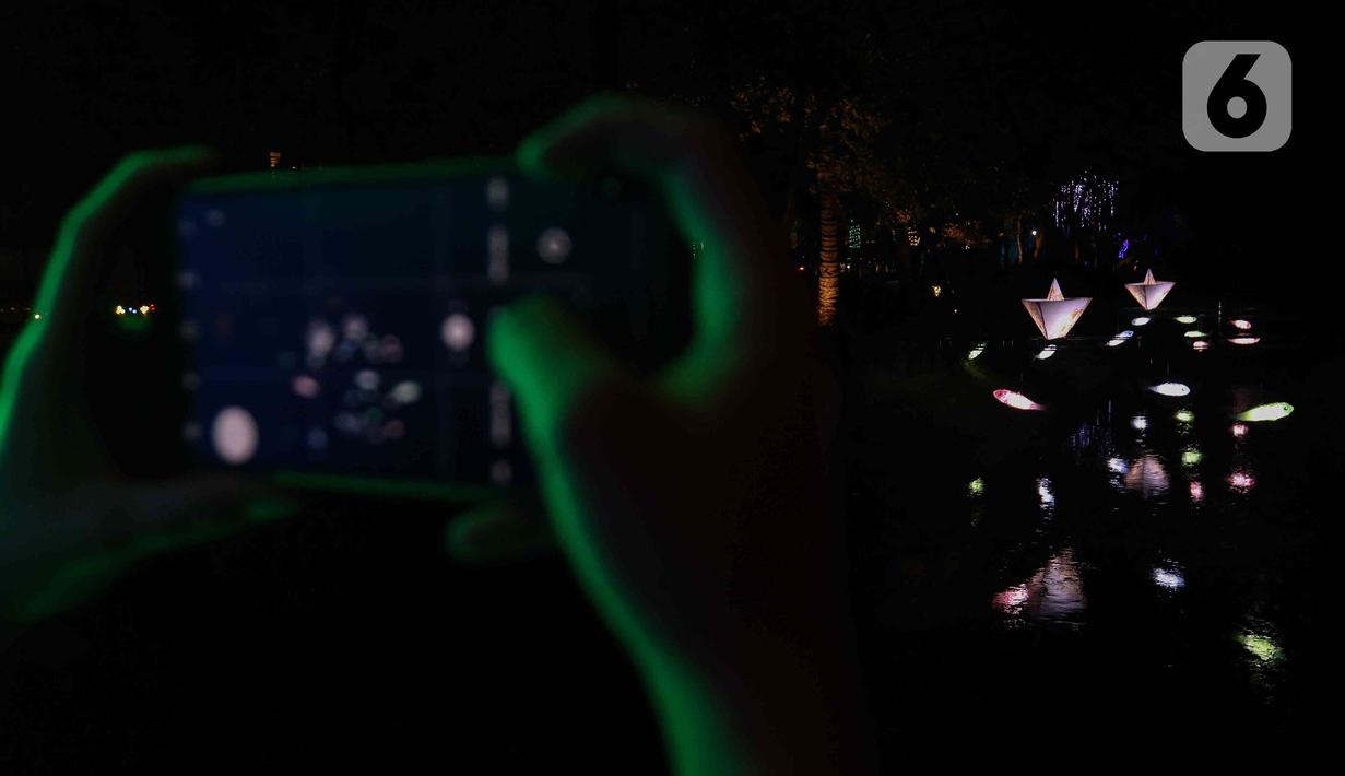 Warga saat memotret Jakarta Lights Festival di Taman Sumenep, Jakarta, Jumat (23/12/2022). Pemprov DKI Jakarta menggelar acara Jakarta Lights Festival sebagai rangkaian perayaan Natal dan Tahun Baru (Nataru) 2023. (Liputan6.com/Herman Zakharia)
