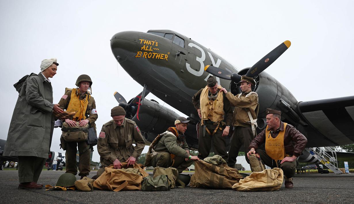 Para peraga Perang Dunia Kedua berpose di samping C-47, sebuah pesawat yang mengangkut pasukan penerjun payung di atas zona penerjunan di Normandia, Prancis, di North Weald Airfield di Epping, sebelah timur London, pada 31 Mei 2024. (HENRY NICHOLLS/AFP)