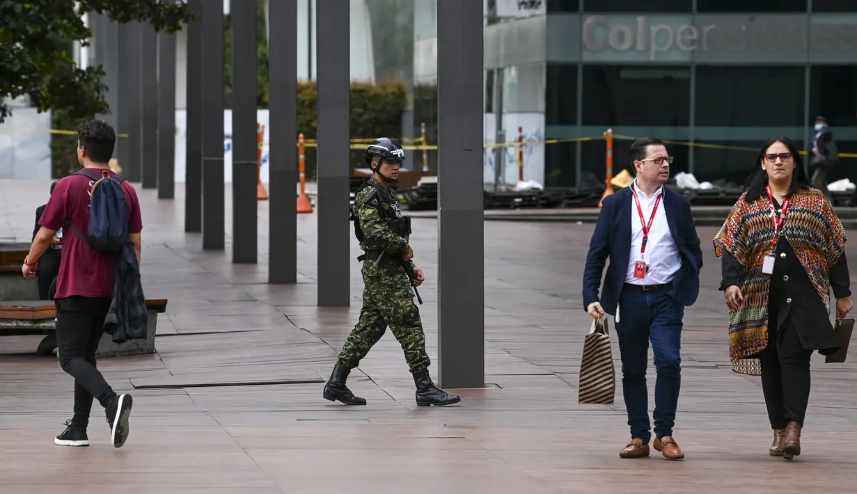 Orang-orang berjalan dekat anggota tentara Kolombia yang sedang berpatroli di dekat kedutaan Israel di Bogota, Rabu (18/10/2023). (Juan BARRETO / AFP)