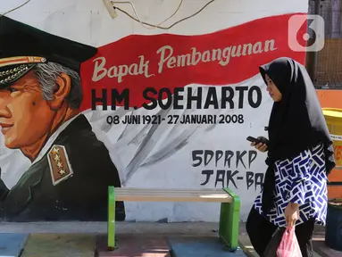 Seorang warga melintasi mural di Kampung Budaya Kawasan Jakarta Barat, Selasa (19/11/2019). Pemprov Jakarta Barat melakukan penataan kawasan pemukiman di beberapa lokasi, salah satunya di Jalan Katalia I Timur. (Liputan6.com/Herman Zakharia)
