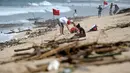 Turis bersantai menikmati Pantai Kuta yang dikelilingi oleh puing-puing dan sampah di Bali, Minggu (9/12). Kawasan pantai Kuta kembali dipenuhi oleh sampah hanyut terbawa oleh gelombang. (SONNY TUMBELAKA / AFP)