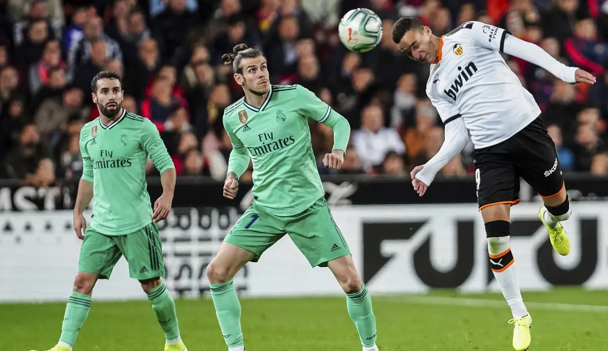 Penyerang Valencia, Rodrigo Moreno berusaha menyundul bola dari kawalan pemain Real Madrid, Gareth Bale dan Dani Carvajal  pada pertandingan lanjutan La Liga Spanyol di Stadion Mestalla (15/12/2019). Madrid bermain imbang 1-1 atas Valencia. (AP Photo/Alberto Saiz)