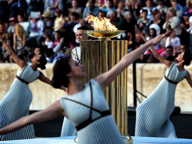 Para penari beraksi di sekitar koldron api olimpiade dalam sebuah upacara penyerahan kepada panitia Olimpiade Rio di Stadion Panathinean, Athena, Yunani, (27/4/2016). (AFP/Aris Messinis)