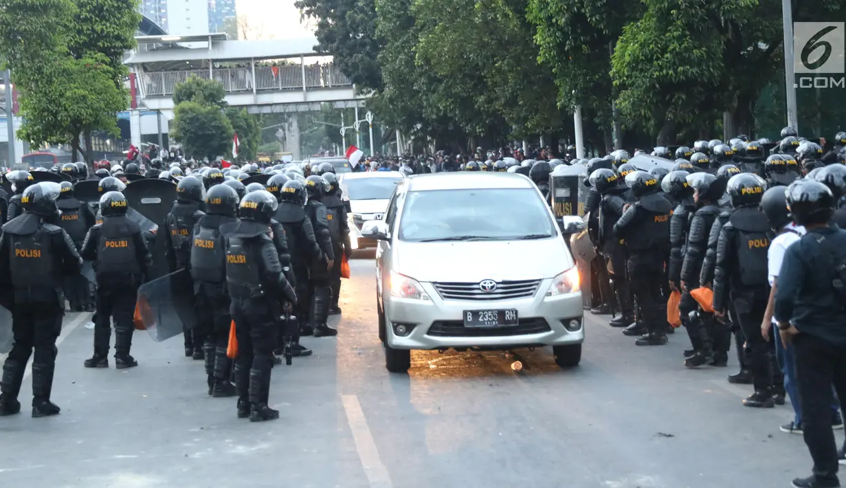 Kendaraan melintas di antara polisi yang berjaga di sekitaran Stasiun Palmerah, Jakarta, Senin (30/9/2019). Jalur di kawasan itu telah dibuka, namun kendaraan harus berhati-hati karena banyaknya batu sisa bentrokan massa di belakang gedung DPR yang berakhir ricuh. (Liputan6.com/Angga Yuniar)