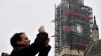 Seorang pria mengambil gambar dengan latar belakang jam Big Ben yang tidak ada jarumnya karena sedang dilakukan perbaikan dan pembersihan di London, Inggris (12/4). (AFP Photo/Ben Stansall)