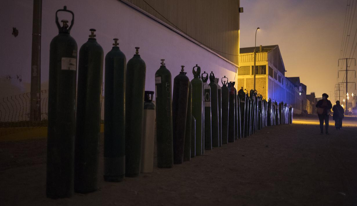 Para wanita berjalan melewati barisan tabung oksigen kosong saat orang-orang menunggu toko buka untuk mengisi tabung mereka di Villa El Salvador, Lima, Peru, Selasa (6/4/2021). Warga Peru terus berjuang mendapatkan oksigen medis untuk merawat pasien COVID-19. (AP Photo/Rodrigo Abd)