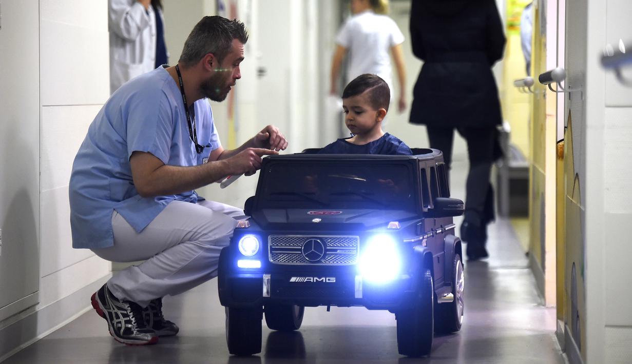 Petugas medis melihat Souvail (2) menggunakan mobil mainan listrik menuju ruang operasi di Rumah Sakit Valenciennes, Prancis, Jumat (2/2). Program ini untuk membuat anak-anak lebih santai sebelum menjalani prosedur operasi. (FRANCOIS LO PRESTI/AFP)