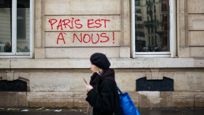 Seorang wanita berjalan melewati grafiti bertuliskan 'Paris adalah milik kita' dekat Arc de Triomphe, Paris, Prancis, Minggu (2/12). Pemrotes kenaikan pajak bahan bakar menandai Arc de Triomphe dengan grafiti berbagai warna. (AP Photo/Kamil Zihnioglu)