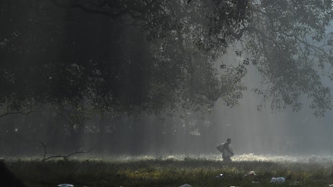 Seorang penjual berjalan mencari pelanggan di pagi berkabut di taman Maidan di Kolkata (29/11/2019). Maidan  merupakan taman bandar terbesar di Kolkata di negeri dalam India di Bengal Barat. (AFP Photo/Dibyangshu Sarkar)