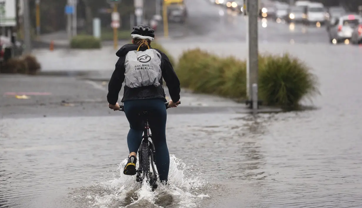Seorang pengendara sepeda melewati banjir di Auckland, Selandia Baru, Rabu (1/2/2023). Peringatan hujan lebat untuk Auckland dicabut, meskipun keadaan darurat tetap berlaku untuk kota terbesar di negara itu setelah rekor curah hujan dan banjir pada hari Jumat menewaskan empat orang orang dan menyebabkan gangguan yang meluas. (Dean Purcell/New Zealand Herald via AP)