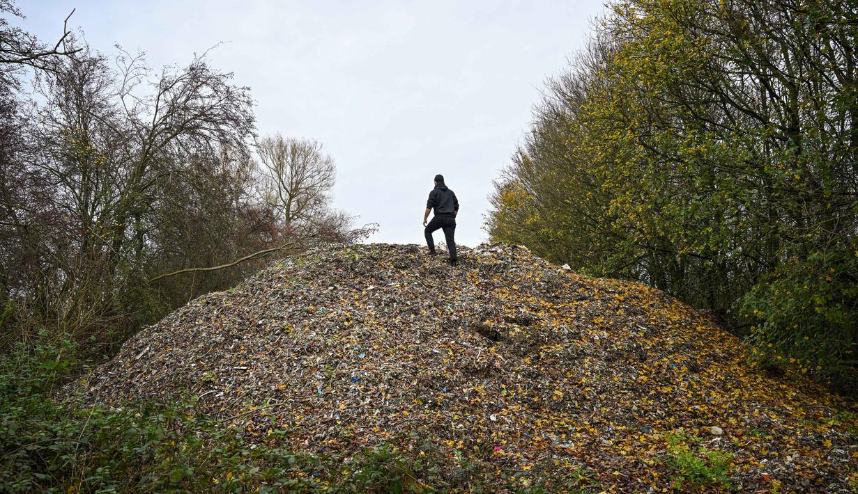 Aktivis lingkungan merekam konten untuk media sosial di tumpukan besar sampah yang dibuang sembarangan, yang ditumpuk di sebuah ladang antara Sungai Cherwell dan Jalan A34 dekat Kidlington, Oxfordshire, di barat London pada 16 November 2025. Gunungan atau tumpukan sampah ilegal berukuran raksasa ditemukan di sebuah ladang di tepi Sungai Cherwell dekat Kidlington, Oxfordshire, Inggris. (Justin TALLIS/AFP)