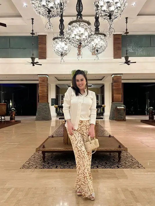 Liburan di Bali, Jennifer Dunn tampil kece memadukan kemeja putih, long pants bermotif, dan tas Dior Lady D-Joy Micro Bag. [Foto: IG/jennifer_haris89].